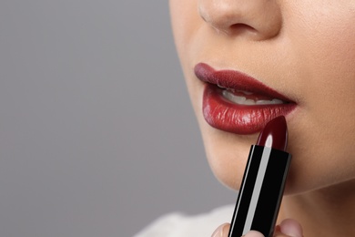 Photo of Beautiful woman applying dark lipstick on gray background, closeup. Space for text