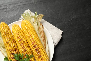 Tasty grilled corn on black table, space for text