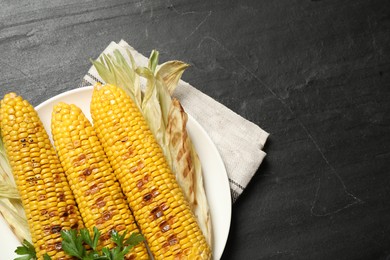 Photo of Tasty grilled corn on black table, space for text