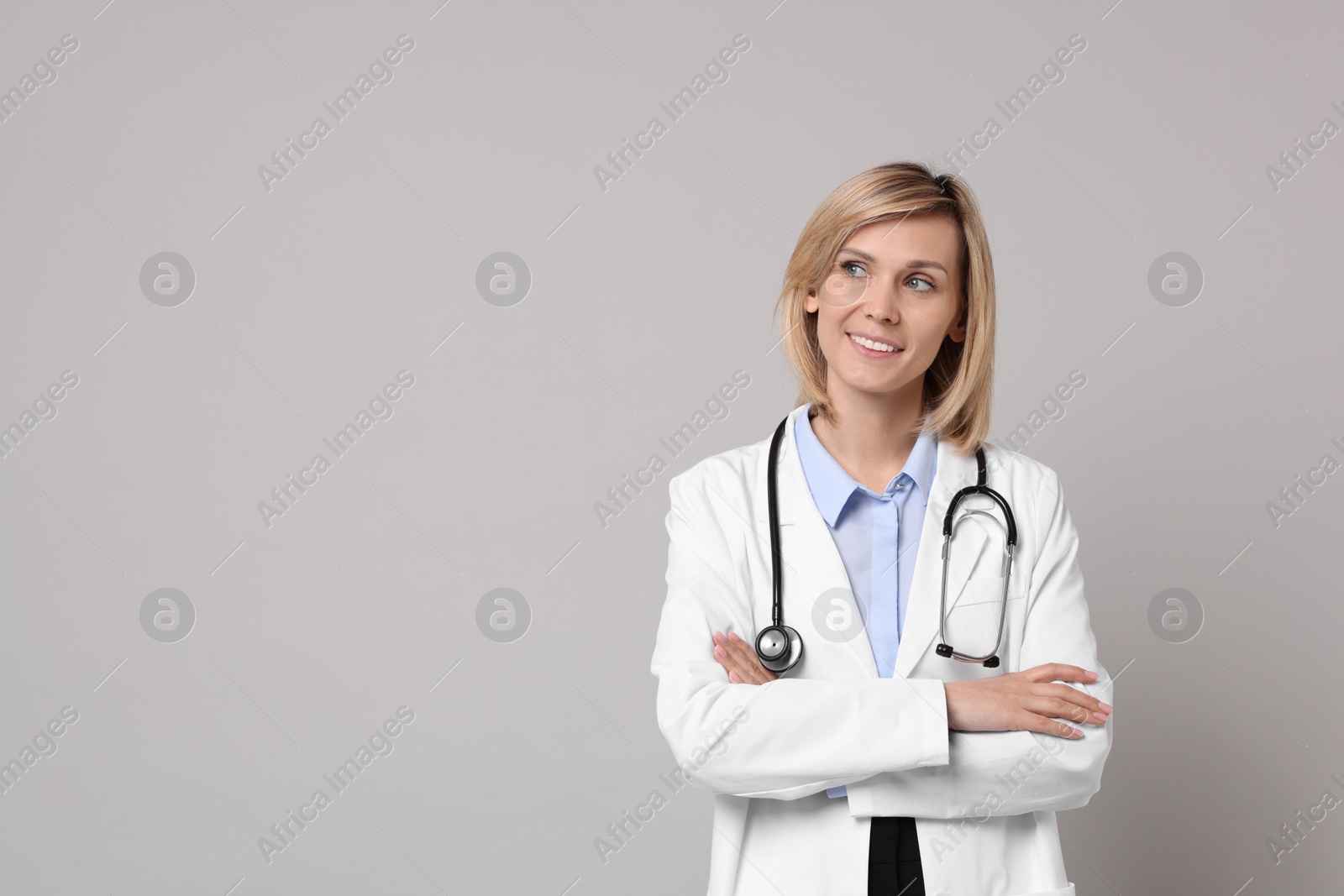 Photo of Smiling doctor with crossed arms on grey background. Space for text