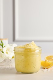Photo of Body scrub in glass jar and lemon on light wooden table, space for text