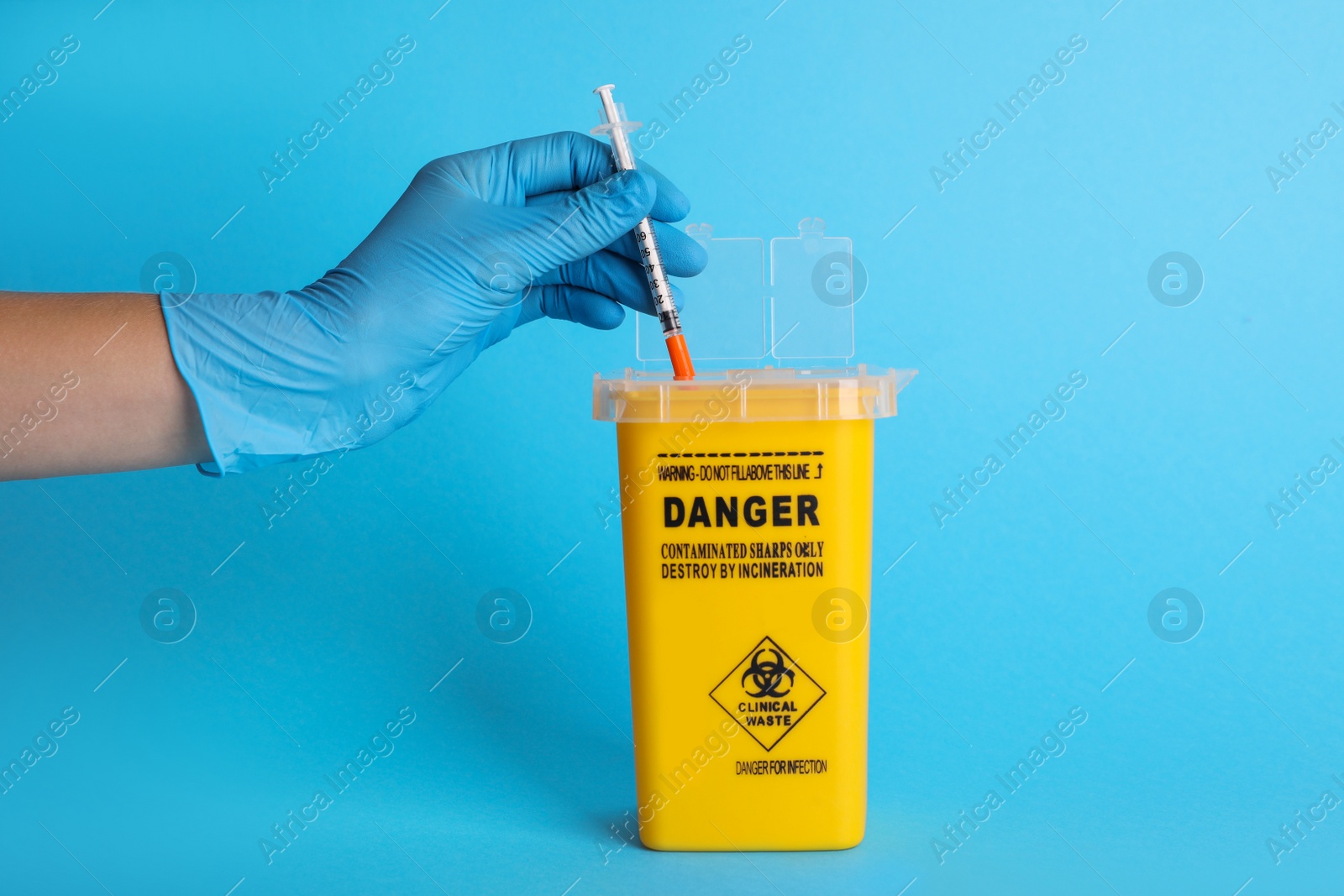 Photo of Doctor throwing used syringe into sharps container on light blue background, closeup