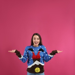 Photo of Surprised young woman in Christmas sweater on pink background, space for text