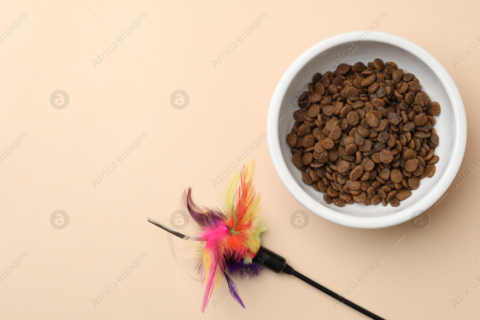 Photo of Dry cat food in bowl and pet toy on beige background, flat lay. Space for text