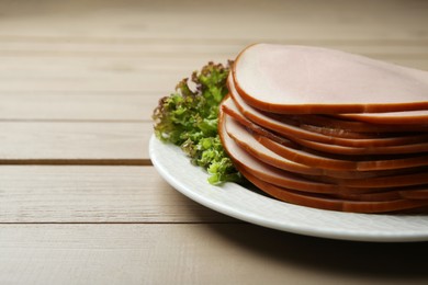 Photo of Slices of delicious boiled sausage with lettuce on beige wooden table, closeup. Space for text