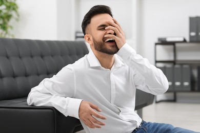 Photo of Handsome young man laughing near sofa in office