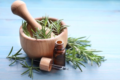 Bottle of rosemary essential oil, mortar with pestle and sprigs on light blue wooden table