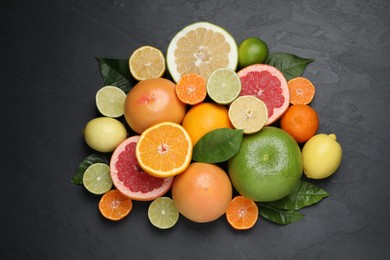 Different ripe citrus fruits with green leaves on black table, flat lay