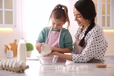Photo of Mother and daughter making dough at table in kitchen