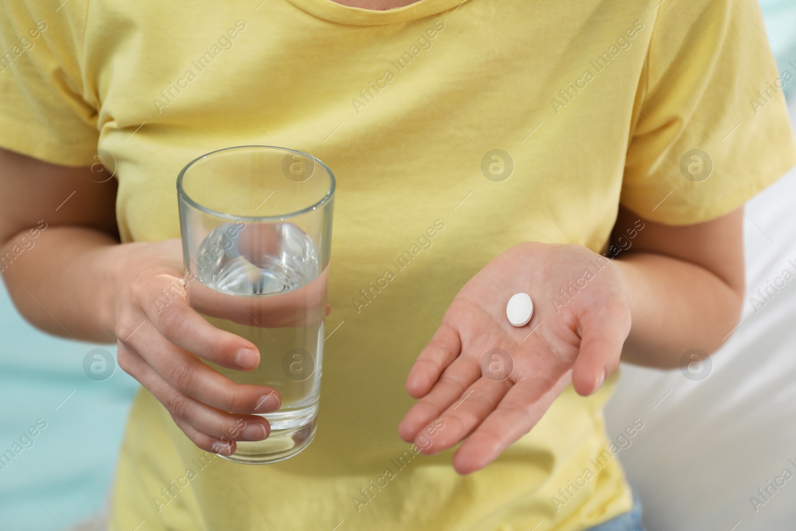 Photo of Young woman with abortion pill and glass of water on blurred background, closeup