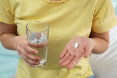 Young woman with abortion pill and glass of water on blurred background, closeup