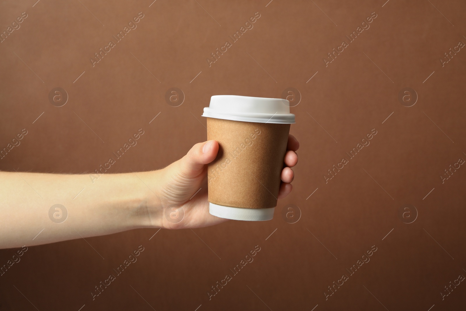 Photo of Woman holding takeaway paper coffee cup on brown background, closeup