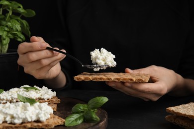 Photo of Woman spreading cottage cheese onto crispy cracker at black table, closeup