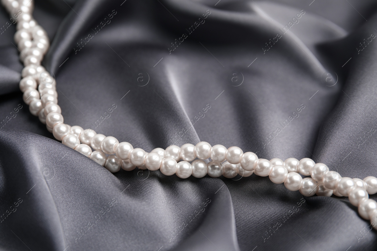 Photo of Beautiful white pearls on delicate grey silk, closeup