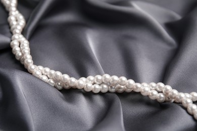 Photo of Beautiful white pearls on delicate grey silk, closeup