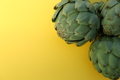 Photo of Whole fresh raw artichokes on yellow background, top view. Space for text