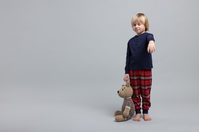 Boy in pajamas with toy bear sleepwalking on light gray background, space for text