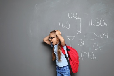 Little school child with backpack and chemical formulas on grey background