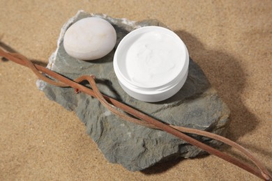 Photo of Jar with cream, stones and branches on sand, above view. Cosmetic product