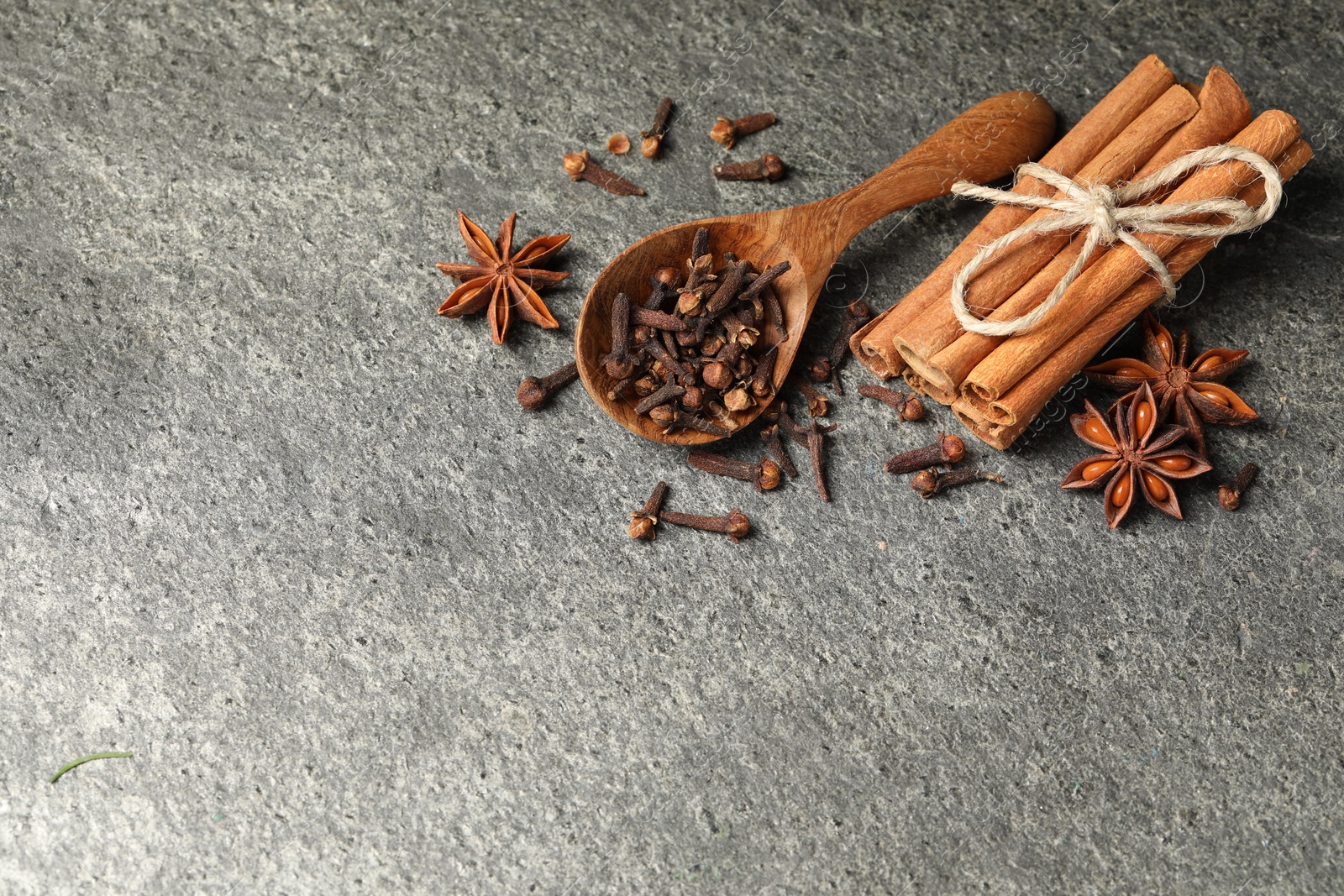 Photo of Wooden spoon with different spices on gray textured table, flat lay. Space for text