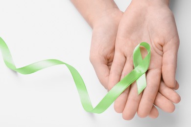 World Mental Health Day. Woman holding green ribbon on white background, top view