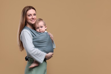 Mother holding her child in baby wrap on light brown background. Space for text