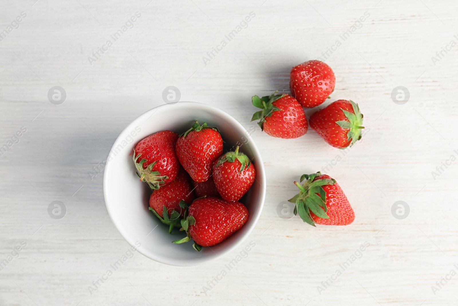 Photo of Ripe red strawberries and bowl on light background, top view