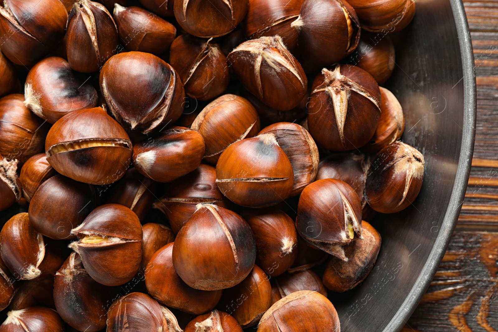 Photo of Delicious roasted edible chestnuts in frying pan on wooden table, top view