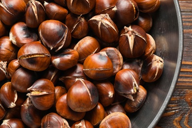 Photo of Delicious roasted edible chestnuts in frying pan on wooden table, top view
