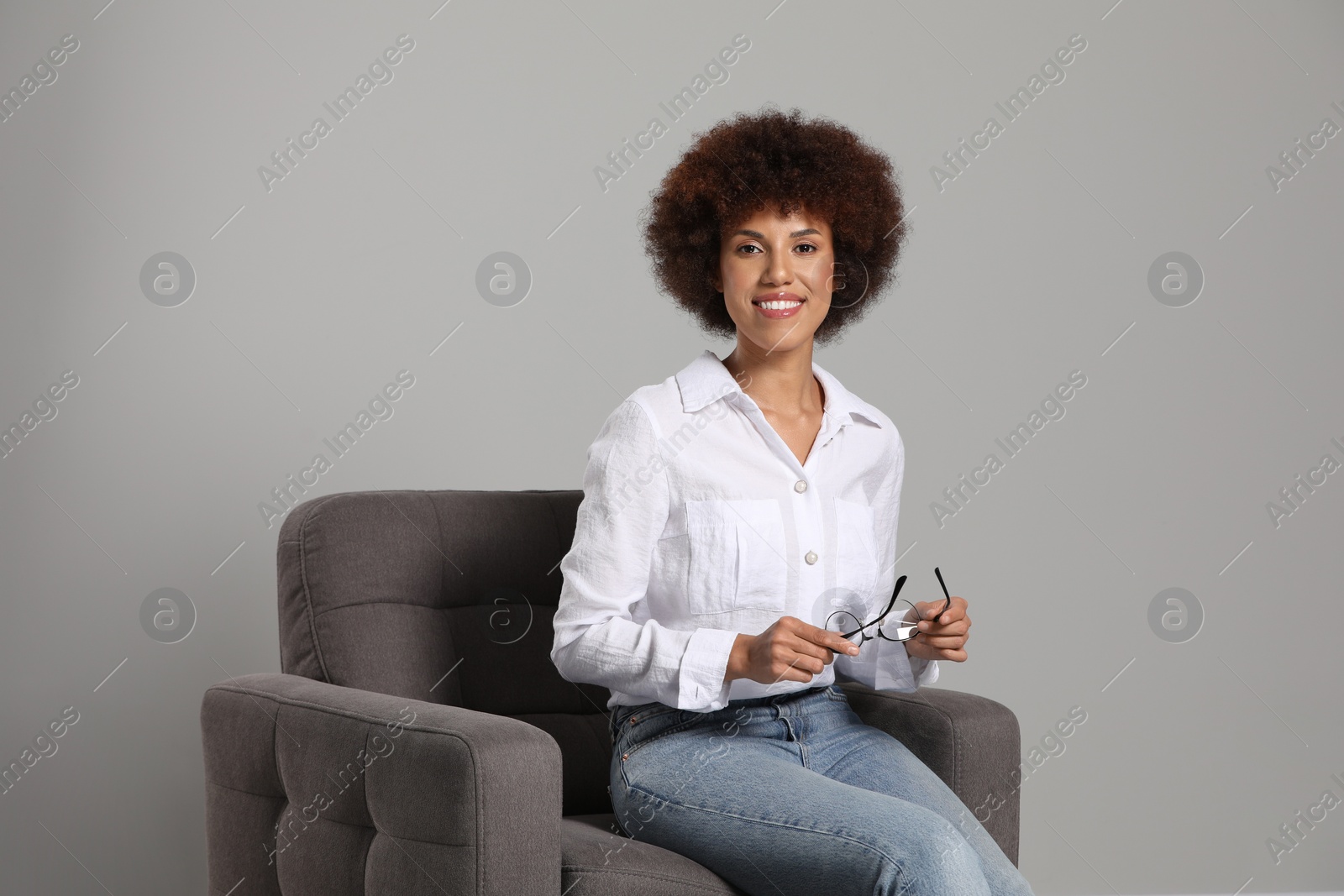 Photo of Beautiful young woman with eyeglasses sitting in armchair on grey background