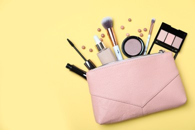 Photo of Cosmetic bag with makeup products and accessories on yellow background, flat lay. Space for text