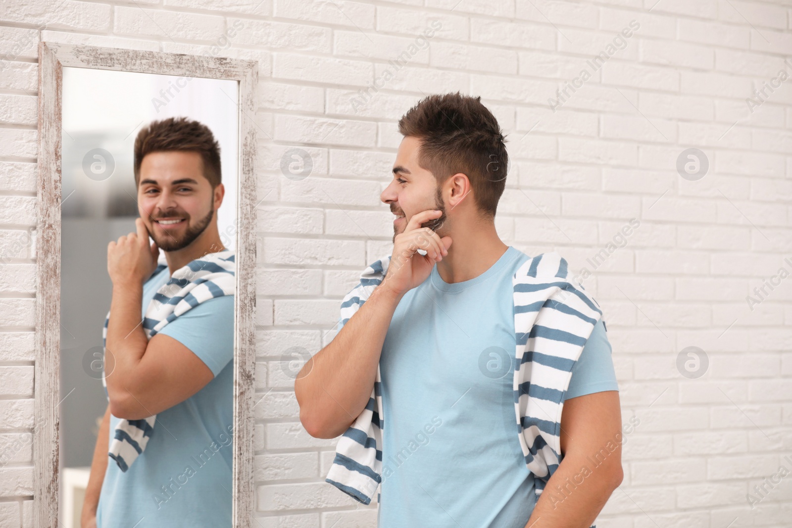 Photo of Young man looking at himself in large mirror at home