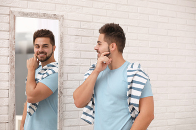 Photo of Young man looking at himself in large mirror at home