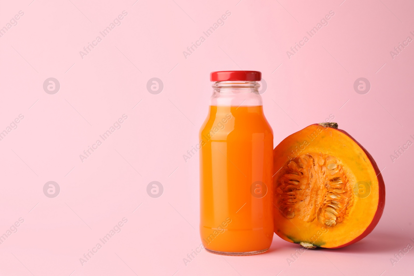 Photo of Tasty pumpkin juice in glass bottle and cut pumpkin on pink background. Space for text