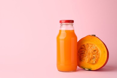 Tasty pumpkin juice in glass bottle and cut pumpkin on pink background. Space for text
