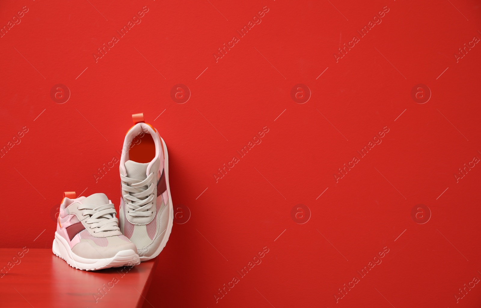 Photo of Stylish women's sneakers on wooden table near red wall, space for text