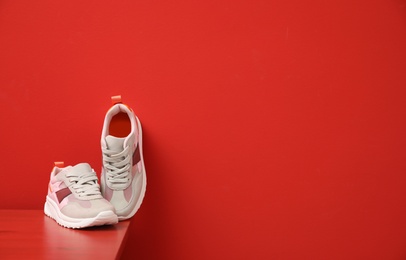 Stylish women's sneakers on wooden table near red wall, space for text