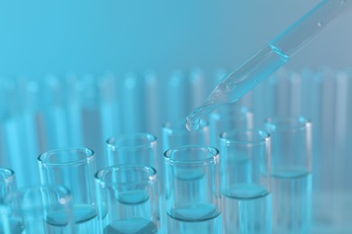 Laboratory analysis. Dripping liquid from pipette into glass test tube on light blue background, closeup