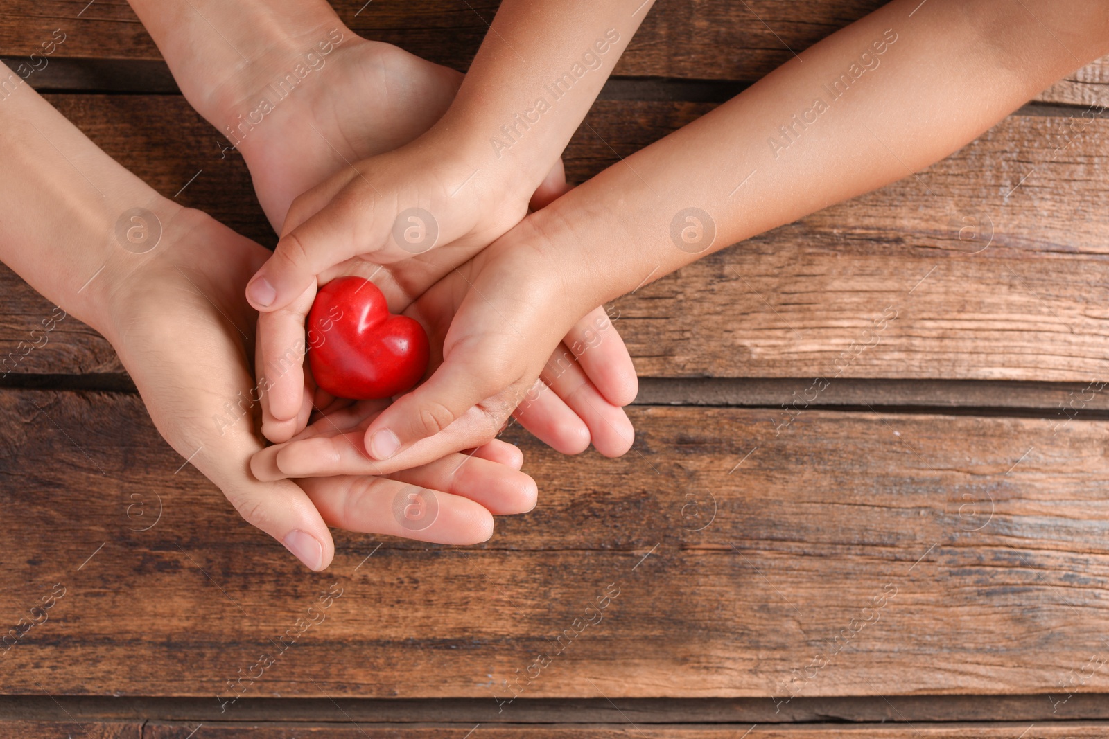 Photo of Family holding small red heart in hands on wooden background