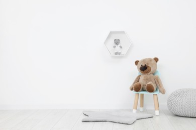 Photo of Teddy bear sitting on chair near white wall in playroom, space for text. Stylish kindergarten interior