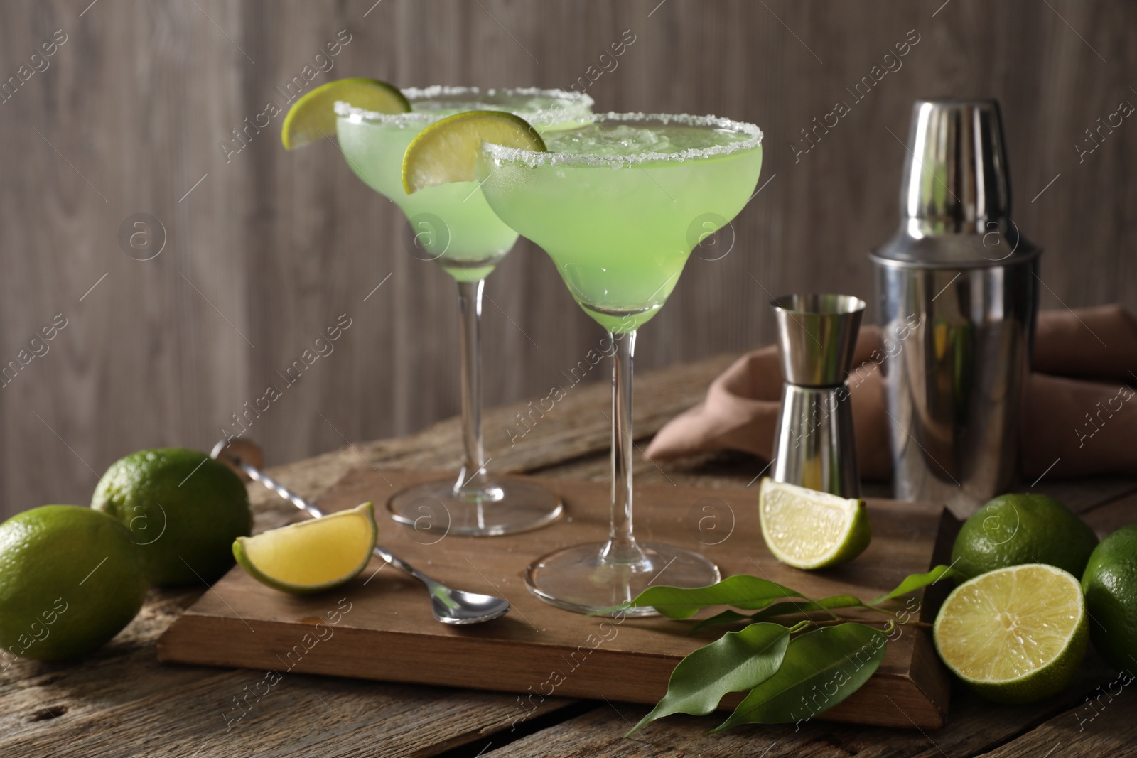 Photo of Delicious Margarita cocktail in glasses, limes and bartender equipment on wooden table