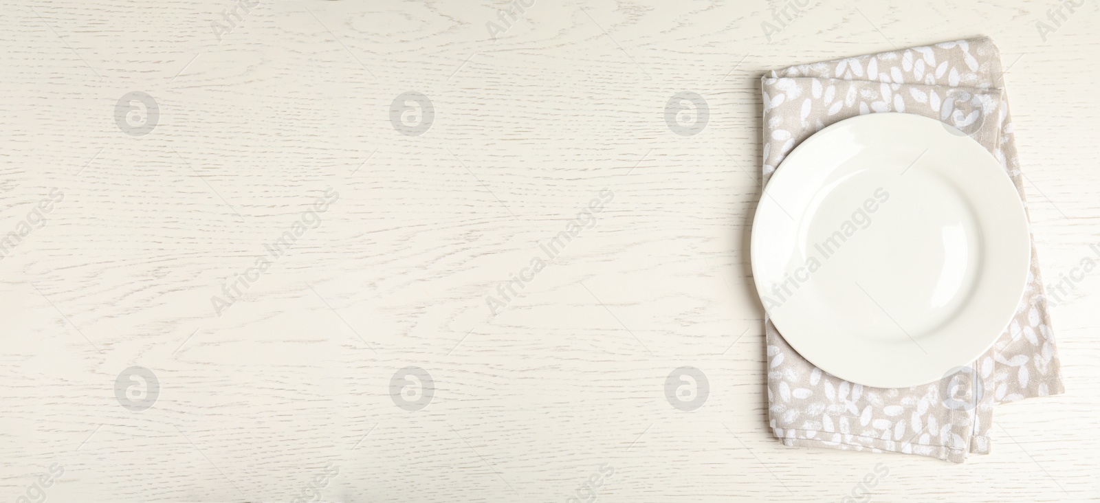 Photo of Empty plate and napkin on white wooden table, top view. Space for text