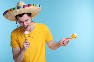 Photo of Young man in Mexican sombrero hat with maracas on light blue background