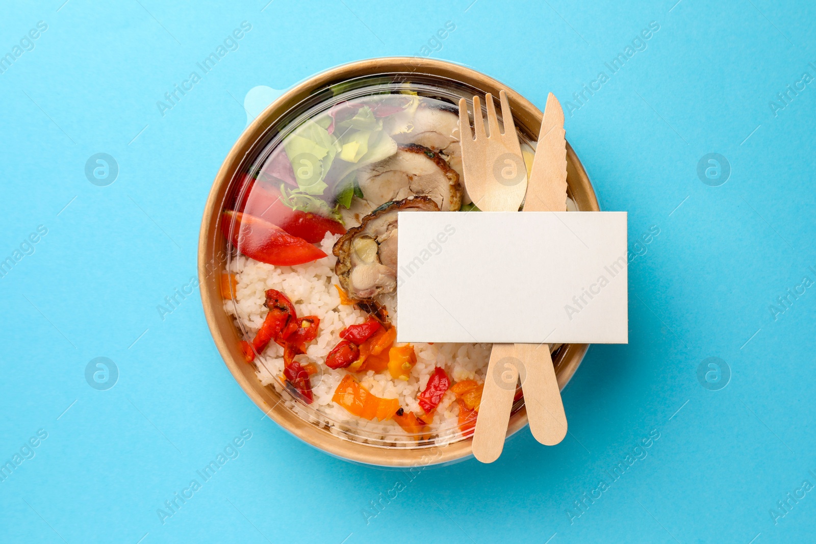 Photo of Tasty food in container with fork and knife on light blue background, top view. Space for text