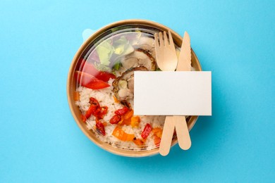 Tasty food in container with fork and knife on light blue background, top view. Space for text
