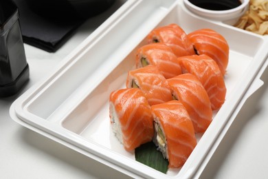 Photo of Delicious sushi rolls with salmon in plastic container on table, closeup. Food delivery