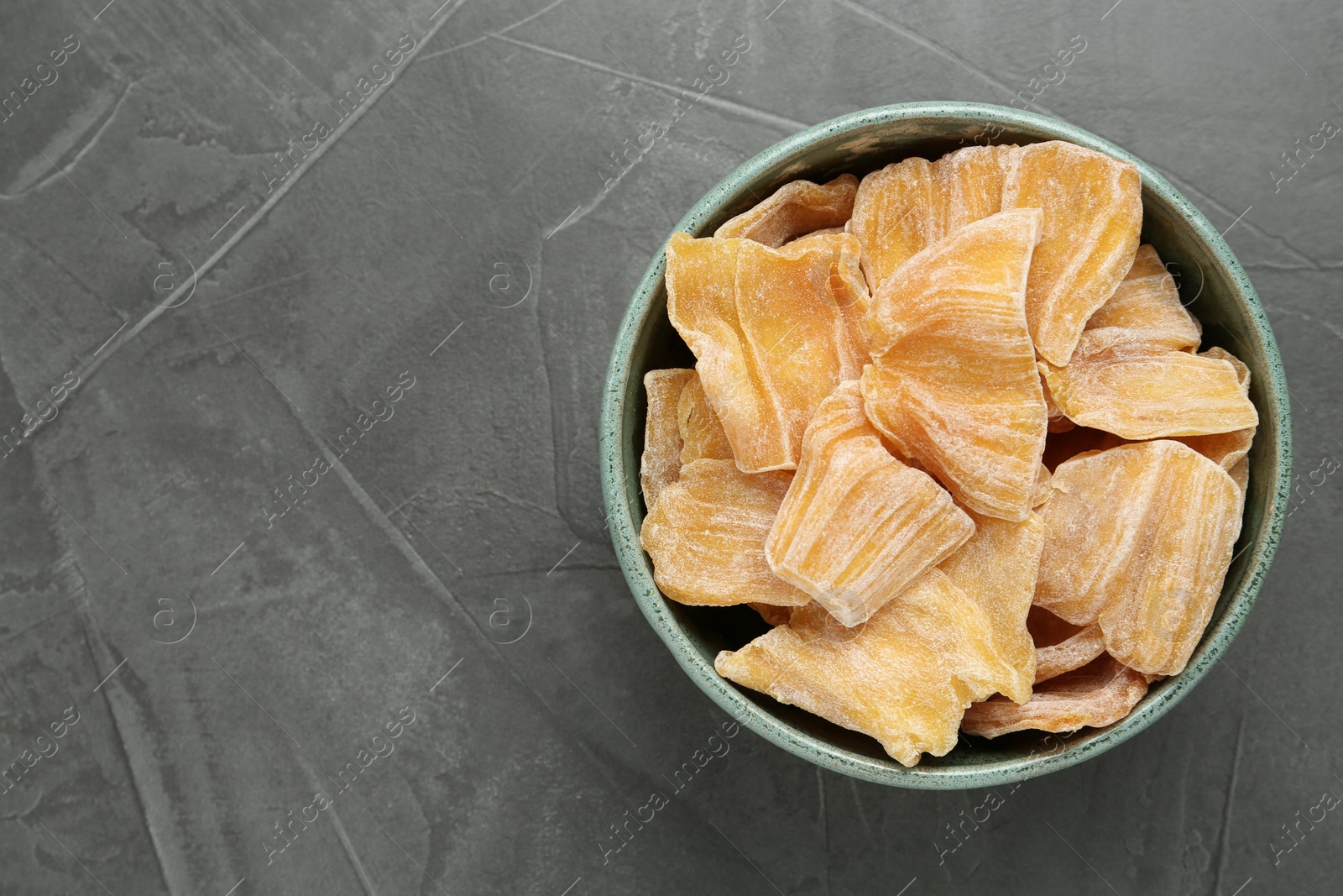Photo of Delicious dried jackfruit slices in bowl on grey table, top view. Space for text