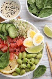 Delicious poke bowl with quail eggs, fish and edamame beans on white wooden table, flat lay