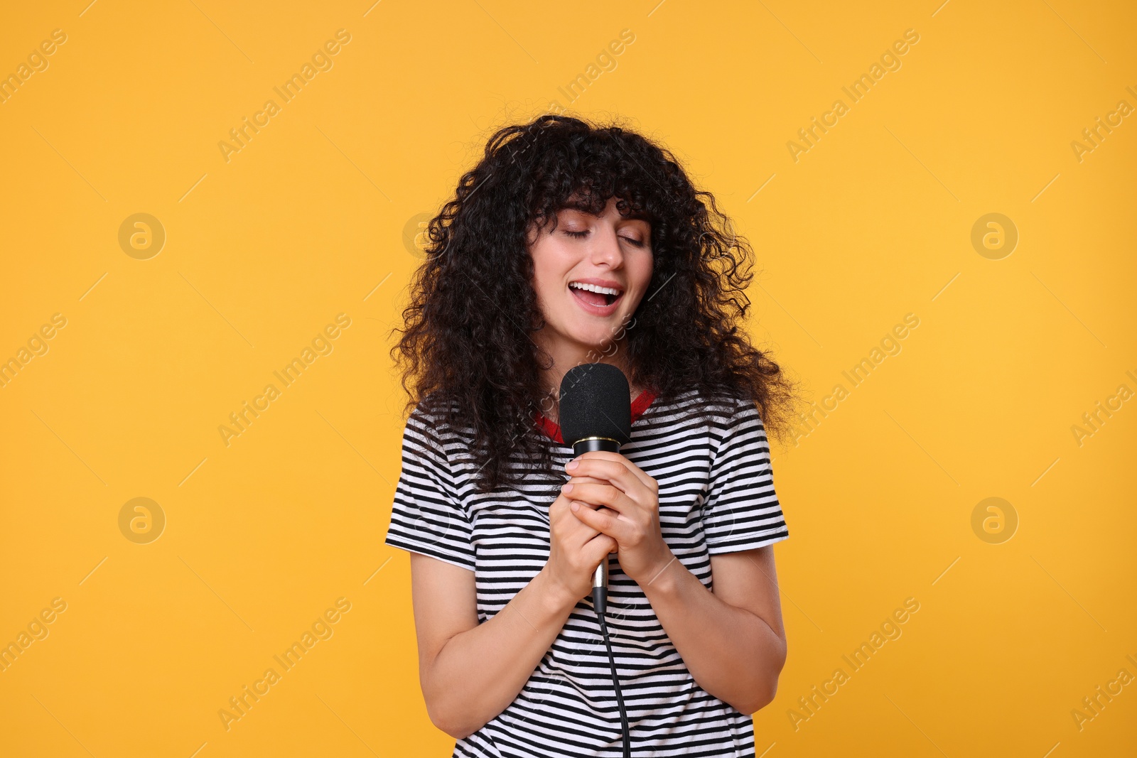 Photo of Beautiful young woman with microphone singing on yellow background