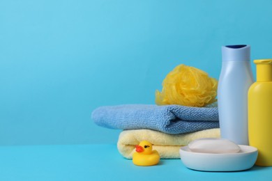 Photo of Baby cosmetic products, bath duck, sponge and towels on light blue background. Space for text